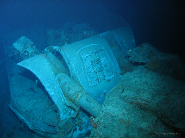 A turret of HMAS Sydney with its gun housing destroyed and the foredeck rent back over the twin gun barrels.