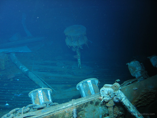 A capstan on the stern of HMAS Sydney, elevated above the collapsed main deck with folded bollards in the foreground.