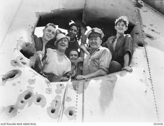 Crew members of the RAN light cruiser HMAS Sydney (II) peer through a hole in the forward funnel. The damage was sustained in action against the Italian Cruiser Bartolomeo Colleoni off Cape Spada, Crete.