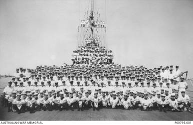 Group portrait of unidentified officers and crew of the RAN light cruiser HMAS Sydney after the successful action against the Italian Cruiser Bartolomeo Colleoni on 19 July 1940. Men are crowded on the deck and stand in the rigging. Ships officers are seated three rows from the front and the only clearly identifiable figure is that of a smiling Captain John Collins, in the centre.