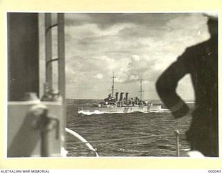OFF SYDNEY, NSW. PORT QUARTER VIEW OF THE HEAVY CRUISER HMAS AUSTRALIA (II) AS SHE APPEARED AFTER HER 1938-1939 REFIT. THE SHIP HAS HAD HER BRIDGEWORK EXTENDED. THE FOUR SINGLE 4 INCH MK V AA GUNS HAVE BEEN REPLACED BY EIGHT TWIN 4 INCH MK XVI WEAPONS ON MK XIX MOUNTINGS. THE OLD 4 INCH GUNDECK HAS BEEN REMOVED AND THE NEW MOUNTINGS PLACED ON THE UPPER DECK. A NEW DIRECTOR CONTROL TOWER HAS BEEN FITTED AND THE ORIGINAL MOVED AFT, REPLACING THE HIGH ANGLE CONTROL POSITION AND THE ORIGINAL CRANE. A SEARCHLIGHT TOWER HAS BEEN ADDED JUST BEFORE IT. HIGH ANGLE CONTROL POSITIONS HAVE BEEN ADDED IN THE BRIDGE WINGS. NEW CRANES HAVE BEEN AMIDSHIPS, PORT AND STARBOARD. THE FOUR SINGLE TWO POUNDER AA GUNS HAVE BEEN REPLACED BY QUADRUPLE 2 POUNDER MOUNTINGS ON PLATFORMS PORT AND STARBOARD JUST FORWARD OF THE SEARCHLIGHT TOWER. HER FORWARD 8 INCH TURRETS AND DIRECTOR ARE TRAINED TO PORT. THE SEAGULL V AMPHIBIAN IS ON ITS CATAPULT. (NAVAL HISTORICAL COLLECTION).