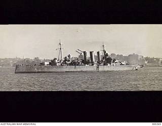SYDNEY, NSW. 1944-03-11. STARBOARD QUARTER VIEW OF THE HEAVY CRUISER HMAS AUSTRALIA (II). THE EXTREMELY DARK GREY COLOUR SCHEME WHICH SHE WORE THE PREVIOUS YEAR HAS EITHER FADED OR BEEN REPLACED BY A SOMEWHAT LIGHTER SHADE, EITHER MS2 OR THE NEWER G10. SHE IS FITTED WITH TYPE 271 SURFACE SEARCH RADAR IN ITS DISTINCTIVE LANTERN MOUNTED IMMEDIATELY ABAFT THE DIRECTOR. A TYPE 284 FIRE CONTROL DIRECTOR IS FITTED TO THE FACE OF THE DIRECTOR. THE AMERICAN SC RADAR PREVIOUSLY CARRIED ATOP HER FOREMAST HAS NOW BEEN REPLACED BY ONE OF THE TWIN AERIALS OF A BRITISH TYPE 281 AIR SEARCH SET. THE OTHER AERIAL IS AT THE HEAD OF A NEWLY RIGGED MAINTOPMAST. BOTH OF HER ORIGINAL POLE MASTS HAVE BEEN REPLACED BY TRIPODS. THE CLOSE RANGE ANTI AIRCRAFT ARMAMENT HAS BEEN AUGMENTED BY THE ADDITION OF TEN 20 MM OERLIKON AA GUNS. TWO ARE MOUNTED IN TUBS ON EACH OF B AND X TURRETS, FOUR ARE MOUNTED PORT AND STARBOARD AMIDSHIPS AND THE REMAINING TWO ARE IN TUBS AT THE BASE OF THE SEARCHLIGHT TOWER. THE CATAPULT AND AIRCRAFT ARE STILL ABOARD ALTHOUGH SOON AFTER THEY WERE LANDED. (NAVAL HISTORICAL COLLECTION).