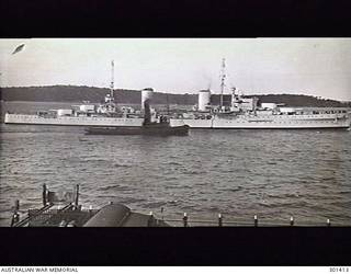 SYDNEY, NSW. C.1937. STARBOARD SIDE VIEW OF THE CRUISER HMAS SYDNEY (II) (EX HMS PHAETON) WITH A TUG ALONGSIDE. NOTE THE SPAR PROJECTING FORWARD OF THE BRIDGE AND THE SINGLE 4 INCH AA GUNS AMIDSHIPS, WHICH DISTINGUISHED THE SYDNEY FROM HER TWO SISTERS HOBART AND PERTH. (NAVAL HISTORICAL COLLECTION)
