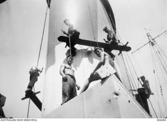 ALEXANDRIA, EGYPT. 1940-07-25. MEMBERS OF THE SHIP'S COMPANY PAINTING THE SHIP'S NEW CAMOUFLAGE SCHEME ON THE AFTER FUNNEL OF THE CRUISER HMAS SYDNEY (II). THE DARK GREY IS PROBABLY 507A, BEING PAINTED OVER THE ORIGINAL LIGHT GREY 507C. (NAVAL HISTORICAL COLLECTION).