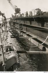 ALEXANDRIA, EGYPT. 1940-07-17. THE CRUISER HMAS SYDNEY (II) SHORED UP IN THE FLOATING DOCK AS THE WATER IS PUMPED OUT. (NAVAL HISTORICAL COLLECTION).