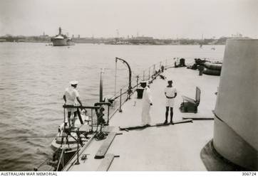 ALEXANDRIA, EGYPT. 1940-08. LIEUTENANT DOLLARD RAN AND LIEUTENANT BAKER RANR ON THE QUARTERDECK OF THE CRUISER HMAS SYDNEY (II). IN THE BACKGROUND IS THE INTERNED FRENCH CRUISER DUGUAY-TROUIN. (NAVAL HISTORICAL COLLECTION).
