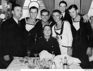 Informal portrait at a welcome home luncheon given to crew members of HMAS Sydney II from the Hunter region, at the Great Northern Hotel. The ship had returned to Sydney from service in the Mediterranean, and on the 11 February the crew had enjoyed a luncheon in Sydney Town Hall following a ceremonial welcome home march through George Street, Sydney. Seated at the table is Mrs Timms, the proprietress of the hotel. Standing, left to right are: unidentified civilian man; unidentified Sydney crew member; unidentified Sydney crew member; unidentified Sydney crew member; possibly S/4212 Able Seaman (AB) Sydney William Harricks in civilian clothing; and 23464 AB Martin Curtis James, of Newcastle, NSW. On 19 November 1941 the Sydney was sunk in the Indian Ocean off the coast of Western Australia by the German auxiliary cruiser Kormoran. All 645 crew members aboard HMAS Sydney were lost. AB James was 19 years of age at the time of his death. AB Harricks was one of the crew members lost when the Sydney sank. The unidentified crew members were also probably aboard the Sydney at the time of its sinking.