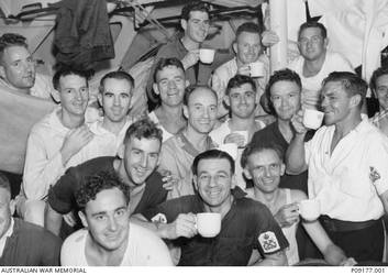 Informal group portrait of petty officers of HMAS Sydney II in the Petty Officers' Mess celebrate their successful action against the Italian cruiser Bartolomeo Colleoni in the Mediterranean. Identified are: 19577 Petty Officer (PO) Henry Joseph Barron Briggs, far left in hammock; 17496 PO Richard Curtis, standing third from left, wearing white singlet; 19385 PO Oliver Ernest Raymond Webb, back, right, holding pole; PO George Berry, front, wearing white undershirt; 19508 PO William Lewis Aylott, centre front, tattoos on left arm; and PO Otto Smith, far right, cup to mouth. On 20 November 1941 Petty Officers Curtis, Webb and Aylott and other unidentified Petty Officers in this photograph were killed in action when HMAS Sydney II was sunk in the Indian Ocean by the German auxiliary cruiser Kormoran. Petty Officers Briggs, Berry and Smith were posted to another ship prior to the sinking of the Sydney.
