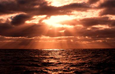 Sunbeams shine through the clouds over water after a storm