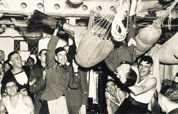 Sailors smiling and laughing in a cabin while lifting one of their crewmates into the air.