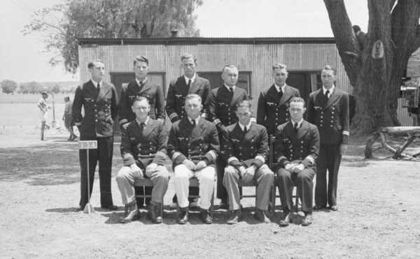 10 German naval officers in uniform, 6 standing behind, 4 seated infront, in an Australian POW camp.
